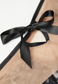 Zwarte kanten lingerie met een doorschijnend nude paneel, voorzien van een satijnen zwarte strik bij de halslijn en delicate randdetails.
