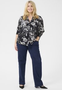 Camicia nera a fiori con bottoni e maniche corte, abbinata a jeans a gamba larga blu scuro e décolleté nere a punta. Design semplice ed elegante.