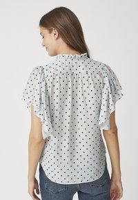 Blusa azzurra con pois neri, maniche corte a volant e scollatura arricciata. Presenta una vestibilità comoda e un orlo curvo.