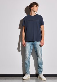T-shirt bleu marine avec une fine rayure horizontale, associé à un jean délavé bleu clair et des baskets blanches. Le tissu a l'air lisse.