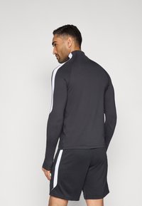 Μαύρο αθλητικό μακρυμάνικο μπλουζάκι με ψηλό γιακά και λευκές ρίγες στο πλάι. Συνδυάζεται με μαύρο σορτς. Λεία, εφαρμοστή υφή.