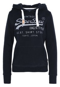 Sudadera azul marino con cordones blancos, bolsillo frontal y texto/logo blanco que dice "Vintage SuperDry Sweat. Shirt. Store Tokio, Japón".
