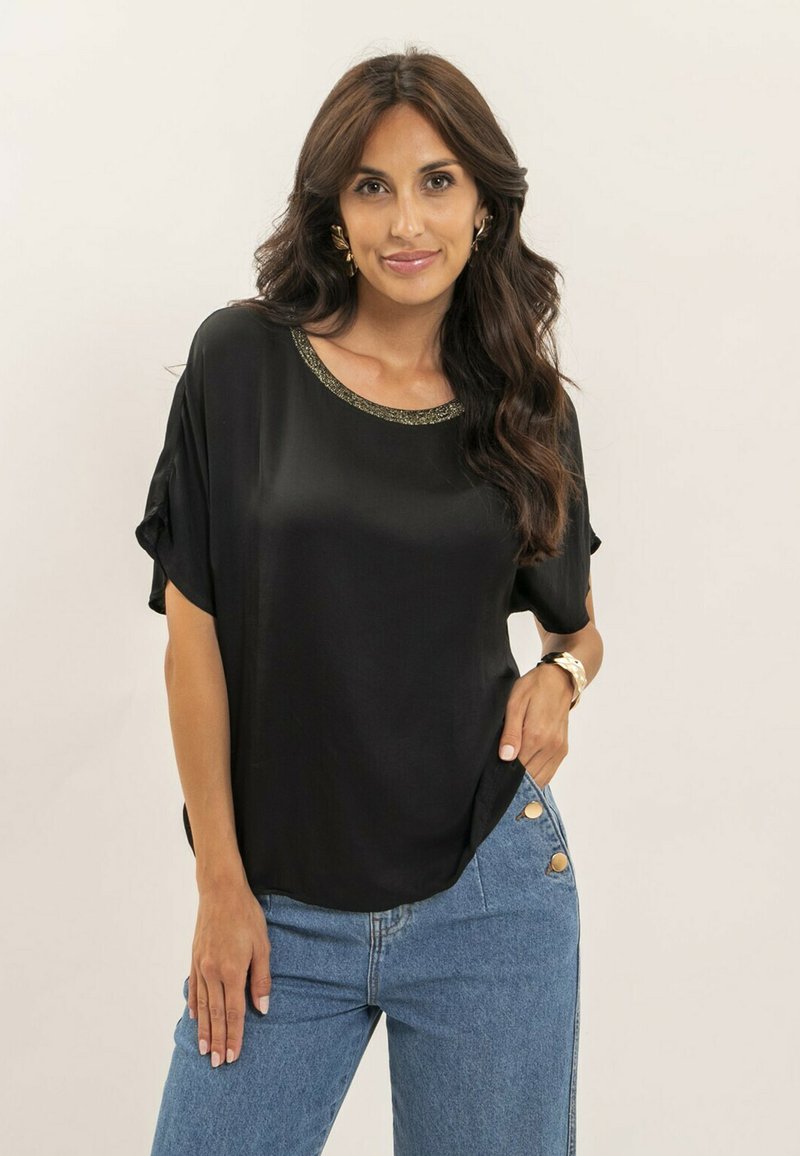 Haut en soie noire avec un col rond ornés d'une bordure dorée, coupe décontractée, manches courtes et texture lisse, accompagné d'un jean taille haute.