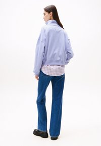 Sudadera oversized de color púrpura claro con cuello alto, combinada con una camisa de cuadros rosa y vaqueros de pierna ancha azules, llevada con zapatos de plataforma negros.