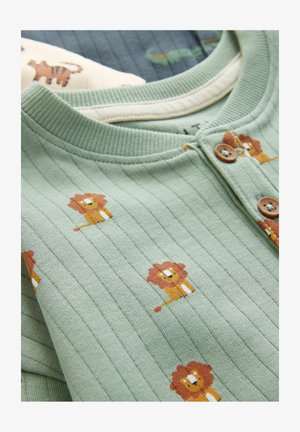 Zeleno rebrasto blago s majhnimi ilustracijami levov v rjavi in rumeni barvi. Vidna je okrogla ovratnica s rjavimi gumbi.