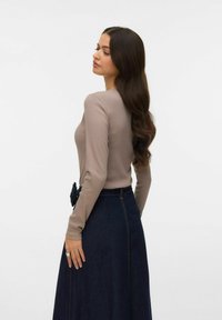 Beige top met lange mouwen gecombineerd met een donker denim rok met een bloemmotief bij de taille. Zachte textuur, strakke pasvorm en hoog getailleerd ontwerp.