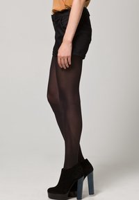 Černé průhledné punčocháče, černé šortky a kotníkové boty s modrým blokovým podpatkem. Outfit je jednoduchý a přiléhavý.