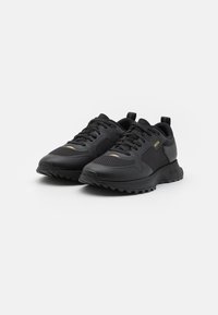 Zwarte sportieve schoenen met een bovenkant van mesh, een gevoerde kraag, een getextureerde zool en gouden accenten. Voorzien van een vetersluiting en merknaam aan de zijkant.