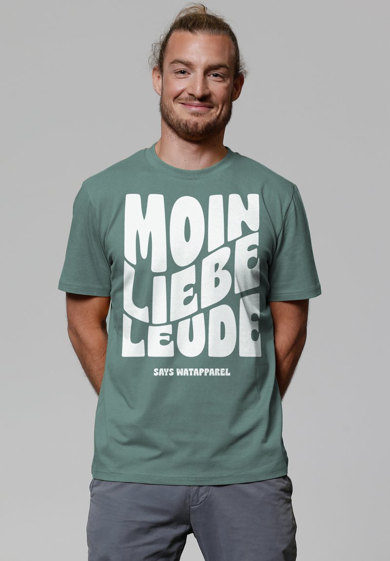 Grünes Baumwoll-T-Shirt mit fettem weißen Text, der "MOIN LIEBE LEUTE" sagt, mit "SAYS WATAPPAREL" darunter. Kurze Ärmel, Rundhalsausschnitt.