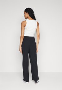 Top blanco sin mangas combinado con pantalones de pierna ancha negros de cintura alta. El conjunto presenta un diseño minimalista y una textura de tela suave.