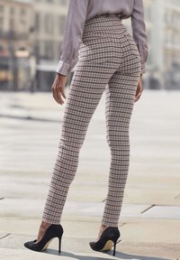 Hoge taille, geruite broek in beige en zwart, aansluitende silhouette, gecombineerd met zwarte hakken. Soepele stoftextuur.