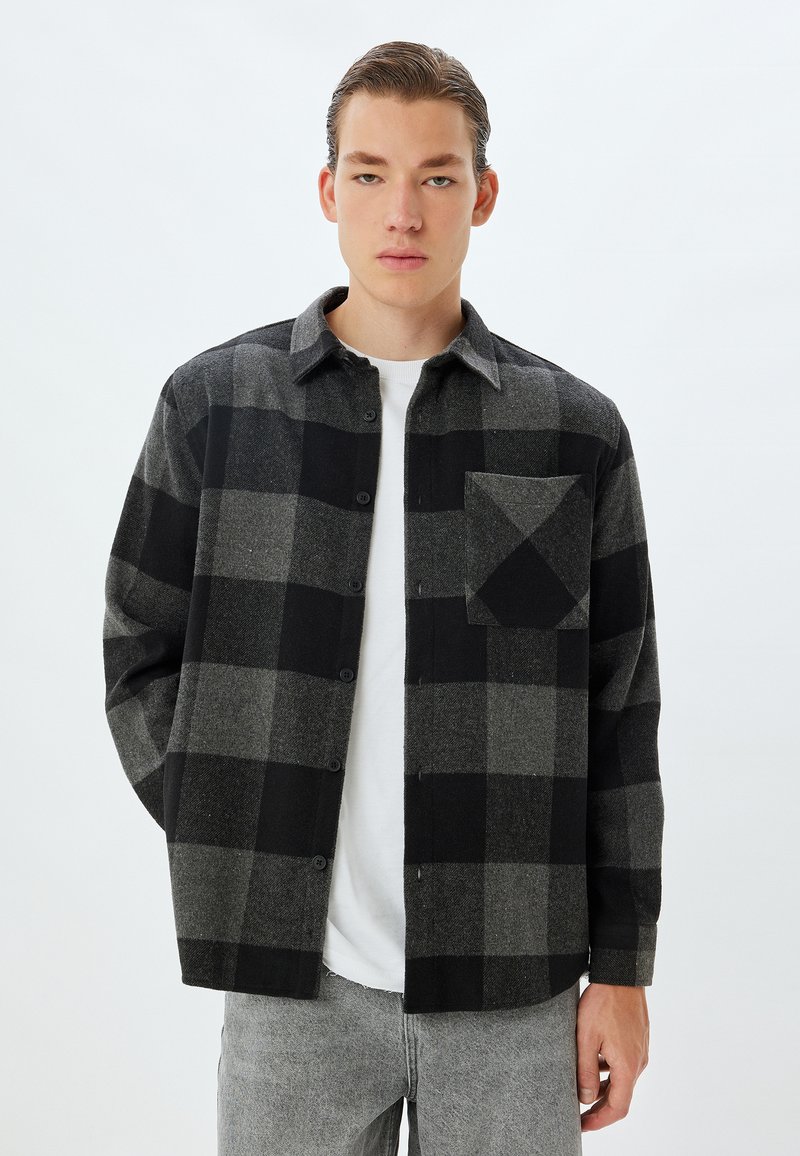 Zwart en grijs geruit shirt van wol, met een knoopsluiting aan de voorkant, kraag en een enkele borstzak met een diagonaal ontwerp.