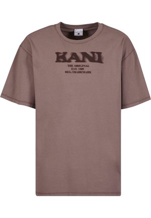 T-shirt marron à manches courtes avec col rond, arborant un texte marron foncé "KANI THE ORIGINAL EST. 1989 REG. TRADEMARK" sur la poitrine.