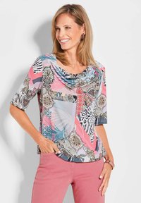 Mehrfarbige Kurzarmbluse mit drapiertem Ausschnitt, die Blumen- und geometrische Muster in Pink, Blau, Grau und Schwarz aufweist. Glatte Stoffstruktur.