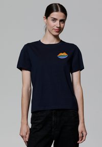 Navyblauwe katoenen t-shirt met korte mouwen, voorzien van een kleurrijk lippenontwerp in oranje, geel, groen en blauw op de borstzak.