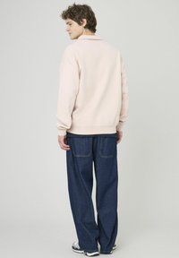 Sweatshirt rose clair avec un col, coupe décontractée et poignets côtelés, associé à un jean en denim large bleu foncé. Design simple, sans motifs.