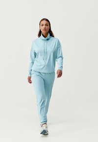 Conjunto deportivo en azul claro que incluye una sudadera con capucha de manga larga, cuello alto y cordones, combinada con pantalones ajustados a juego y zapatillas.