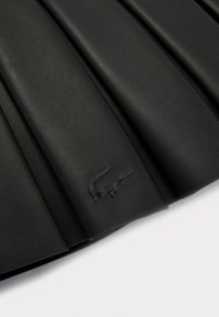 Svart skinn plissert skjørt med en subtil preget krokodillelogo. Jevn tekstur og skreddersydd design med presise folder.