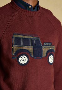 Bordový pletený sveter s vyšitým vintage terénnym vozidlom v hnedej a námorníckej modrej farbe na tmavom károvanom tričku.