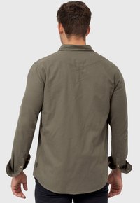 Camisa de manga larga verde oliva con puños abotonados, dobladillo curvado y textura suave, vista desde la parte de atrás.