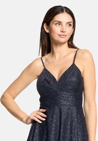 Robe bleu marine sans manches avec un décolleté triangulaire, un corsage plissé et des sequins scintillants dispersés, créant un effet de scintillement texturé.