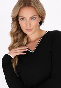 Top negru cu maneci lungi, design cu decolteu în V și margine albă pe decolteu și mansete. Textură netedă cu o siluetă ajustată.