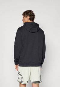 Sort hætte-sweatshirt med en afslappet pasform, der har en kængurulomme og ribbede manchetter. Bæret over lysfarvede mesh-shorts.