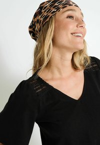 Haut noir à col en V avec des manches courtes, présentant des détails en dentelle aux épaules et un bandeau beige à imprimé léopard. Texture lisse.