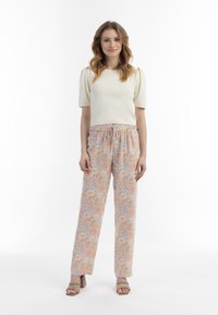 Lichtbeige geribde top met korte pofmouwen; bloemenpatroon, pastel brede broeken met een elastische tailleband. Draagt een paar beige haksandalen.