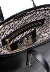 Interno di una borsa a mano in pelle nera con fodera stampata, dotato di tasche con zip, accessori in tonalità oro e un logo decorativo in argento.