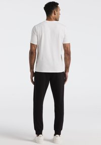 Witte korte mouwen t-shirt, gladde textuur, gecombineerd met zwarte joggingbroek, tapered fit, elastische manchetten, en witte sneakers met branding.