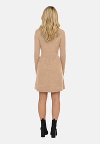 Knutklänning i ljusbeige, med ribbad textur, långa ärmar, figursydd midja och utsvängd kjol, tillsammans med svarta klackade ankelboots.