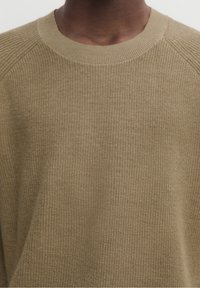 Beige stickad tröja med ribbad textur, rundad halsringning och raglanärmar, med en mjuk och bekväm tygfinish.