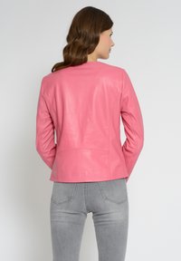 Pink læderjakke med en skræddersyet pasform, glat tekstur og minimale syninger. Bæres over grå jeans med et enkelt kravedesign.
