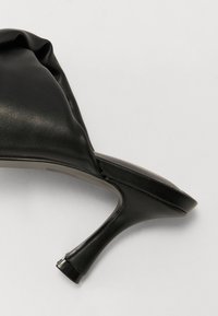 Sandal alta nera con tacco, realizzata in pelle liscia, caratterizzata da un design della parte superiore drappeggiato e un tacco sottile e curvo. La suola sembra piatta.
