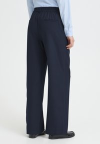 Pantalon large bleu marine avec taille élastique et poches latérales, présentant une texture lisse et un design ajusté.