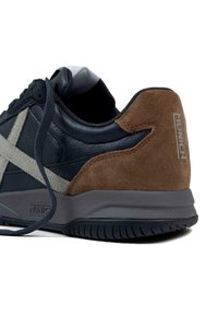 Sneaker neri e marroni realizzati in materiali scamosciati e in pelle, con un accento grigio e suola testurizzata. Logo sulla parte posteriore.