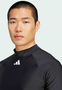 Zwart sportshirt met een hoge hals, gemaakt van glad materiaal, met een wit logo op de borst en contrasterende naden.