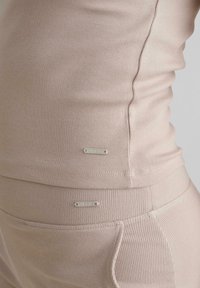 Beige ribbet tanktop og leggings med diskrete brandtags, tætsiddende design og blød tekstur, der viser et sømløst look.