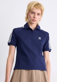 Polo bleu marine avec un col, deux boutons et des accents blancs à trois rayures sur les épaules. Présente un petit logo blanc sur la poitrine.