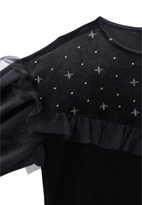 Czarna aksamitna bluzka z tiulowymi falbanami, ozdobiona srebrnymi gwiazdkami, z teksturowanym wykończeniem. Posiada okrągły dekolt i krótkie rękawy.