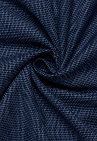 Tessuto blu scuro con un motivo tessuto in modo compatto, attorcigliato al centro, che mostra dettagliata struttura delle fibre e pieghe.