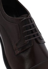 Bruine leren schoen met een textuurstofpaneel, ronde neus en standaard veters. Gladde afwerking met subtiele stikdetails.