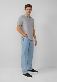 Polo gris à manches courtes, associé à un jean droit bleu clair et des baskets noires. Texture lisse, design décontracté.