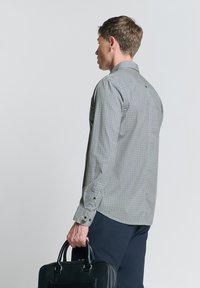 Geruite lange mouw blouse in grijs en wit, met een button-down kraag en manchetten met twee knopen, gecombineerd met een zwarte leren aktetas.