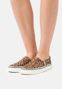 Lepardmönstrade slip-on skor med en ovandel i brunt kanvas, vit gummisula och elastiska sidodetaljer för enkel påtagning.