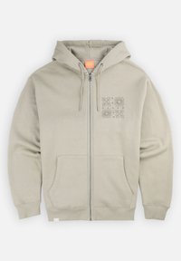 Hoodie beige zippé avec capuche à cordon de serrage, poches avant et un design graphique imprimé sur la poitrine gauche. Tissu en mélange de coton, texture lisse.