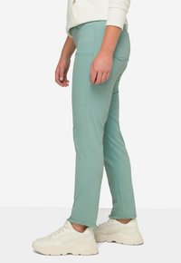 Jeans elásticos verde claro con un ajuste ajustado, que cuentan con bolsillos delanteros y detalle de dobladillo deshilachado, combinados con zapatillas deportivas blancas de suela gruesa.