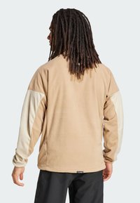 Polarowa bluza w jasnobrązowym kolorze z kremowymi rękawami, o luźnym kroju i miękkiej fakturze. Zawiera metkę u dołu.