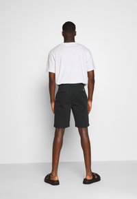 Černé kraťasy s rovnými nohavicemi a ohrnutými lemy, s zadními kapsami, v kombinaci s jednoduchým bílým tričkem a černými sandály.